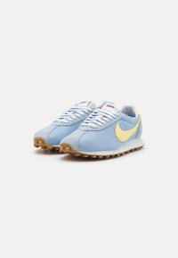 Svijetloplavi mrežasti i antilop tenisice s žutim Swoosh-om, bijelim vezicama i gumeni potplat s uzorcima za prianjanje. Crveni logo na jeziku.