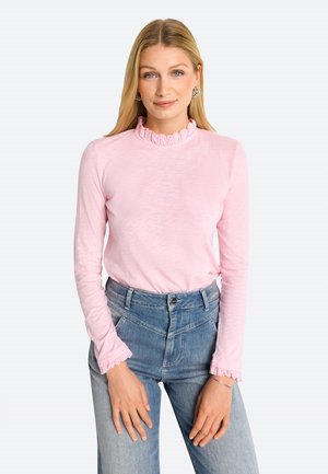 Hellrosa Langarmhemd mit gerafftem hochgeschlossenem Kragen und Manschetten, kombiniert mit blauen hochtaillierten Denim-Jeans mit vorderen Taschen.