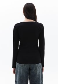 Schwarzes Longsleeve-Oberteil mit rundem Halsausschnitt. Weicher Stoff und taillierte Passform, kombiniert mit verblassten blauen weitgeschnittenen Jeans. Einfacher, klarer Stil.