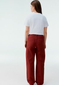 Pantaloni larghi color bordeaux in cotone con cuciture visibili e due tasche posteriori. Abbinati a una maglietta bianca semplice.