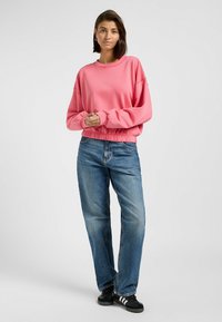 Roze sweatshirt met geribde zoom en mouwen, gecombineerd met blauwe rechtgaande jeans en zwarte sneakers met witte strepen. Gladde stof textuur.