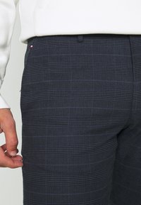 Pantaloni a quadri blu navy in tessuto testurizzato, con un motivo sottile. Progettati con una vestibilità standard e una cintura standard, arricchiti da una mano visibile.