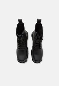 Botas de tobillo de cuero negro con un acabado suave, diseño con cordones, tirador y suela gruesa. Cuenta con un collar acolchado para mayor comodidad.