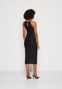 Vestido negro midi con diseño de abertura en la espalda, hecho de tela de punto acanalado, forma ajustada, llevado con zapatos de tacón negros.
