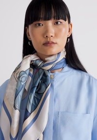 Siidist sall, millel on geomeetrilised mustrid sinise ja valge tooni, kantud kaela ümber isikul, kes on riietatud helesinisesse särki.