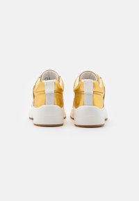 Gula metalliska sneakers med en vit gummisula och texturerad detalj på hälen med en kontrasterande tygremsa.