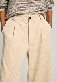 Beige corduroy wide-leg trousers with front pleats, side pockets, and a button closure, featuring a textured ribbed pattern.