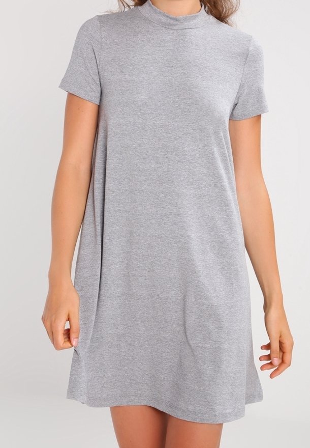Femme portant une robe décontractée gris clair à manches courtes et col montant, debout les bras détendus le long du corps.