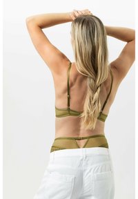 Soutien-gorge vert olive avec bretelles réglables et accents en maille, associé à un pantalon blanc taille haute. Le dos présente un design découpé.