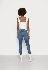 Höga mörkblå skinny jeans med två bakfickor. Matchas med en vit tanktop med fyrkantig halsringning och ljusa ankelstövlar.