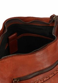 Bruine leren tas met een ritssluiting, een gladde textuur en een geweven accent. De binnenvoering is van stof en bevat een extra zak.