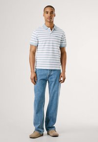 Polo tričko s horizontálnymi pruhmi v svetlomodrej a bielej farbe, krátke rukávy a golier. V kombinácii so svetlomodrými džínsami a béžovými nazúvacími topánkami.