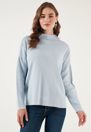 Suéter azul claro con cuello alto, mangas largas, textura acanalada y corte holgado, combinado con jeans oscuros. Sin patrones ni acentos notables.