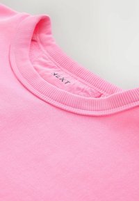 Hele roosa pusa, millel on ümara soonikkoega kaelus ja pehme tekstuur. Sildil kaeluses on kirjas "NEXT".