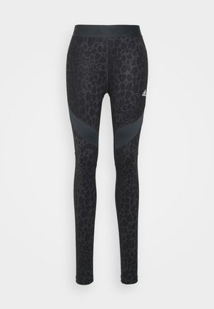 Leggings noirs imprimés avec un motif léopard, fabriqués en tissu extensible, avec une large taille et des accents noirs angulaires au niveau des cuisses.