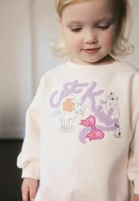 Felpa rosa chiaro con gatti ricamati, fiocco rosa e scritta viola, con polsini a coste e scollo rotondo.