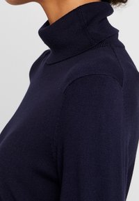 Maglione a collo alto di colore blu navy con un design aderente, scollo a coste e texture morbida. Vista ravvicinata che mette in risalto i dettagli della cucitura sulla spalla.