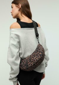 Borsa a spalla con stampa leopardata in marrone scuro e nero, forma curva, tessuto morbido, tracolla regolabile e dettaglio di chiusura a scatto ben visibile.