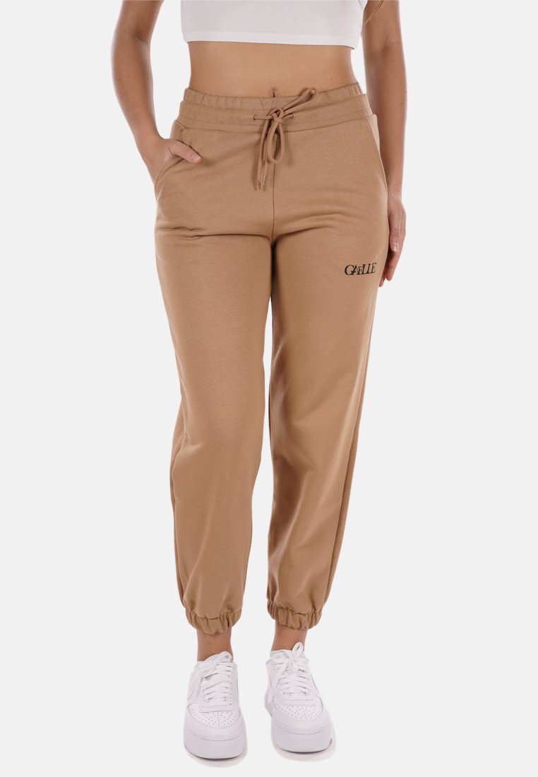 I pantaloni da tuta beige con cintura elastica presentano un cordoncino, polsini alle caviglie e la parola "GILLE" ricamata in nero sulla coscia sinistra.