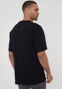Sort kortærmet t-shirt med rund halsudskæring, lavet af bomuld. Stoffet ser blødt og glat ud med en afslappet pasform.