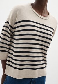 Maglione beige con righe orizzontali nere, vestibilità ampia, scollatura tonda e maniche a tre quarti. Orlo a coste e texture morbida.