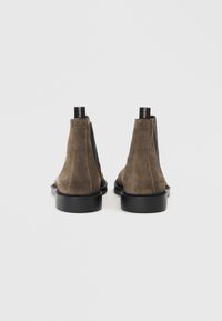 Botines de ante marrón con paneles laterales elásticos y una pequeña tira en la parte posterior, presentan una suela de goma negra y una textura suave.