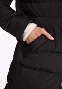 Czarna kurtka puchowa z pikowaną teksturą i boczną kieszonką. Rękaw ma widoczny biały ściągacz.