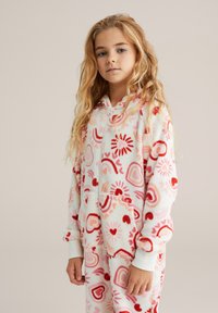 Mameluco de vellón blanco con patrones de corazones y remolinos en rosa y rojo, cremallera frontal y dos bolsillos; forrado con puños y dobladillo acanalados.