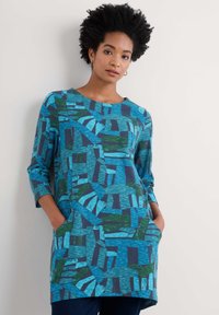 Långärmad tunika i nyanser av blått och grönt, med ett geometriskt mönster och sidofickor, tillverkad av ett mjukt, texturerat tyg.