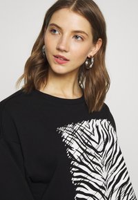 Sweatshirt preto com um ousado design de riscas de zebra brancas de um lado. Feito de um tecido macio com um corte descontraído e decote largo.