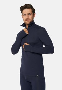 Marineblaues, langärmliges Sportshirt mit hohem Kragen, Daumenlöchern und einem Reißverschluss vorn, aus einem strukturierten, feuchtigkeitsableitenden Stoff.