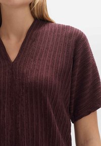 Haut bordeaux avec un décolleté en V, manches courtes, rayures verticales texturées et une finition en tissu doux.