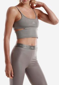 Top sportivo a collo alto e leggings aderenti in morbido tessuto grigio chiaro. Il reggiseno presenta ritagli sui lati; la cintura ha un dettaglio con logo.