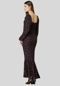 Abito nero con stampa floreale, maniche lunghe e fondo svasato. Presenta un retro arricciato e scollatura aperta. Il tessuto ha una consistenza morbida.