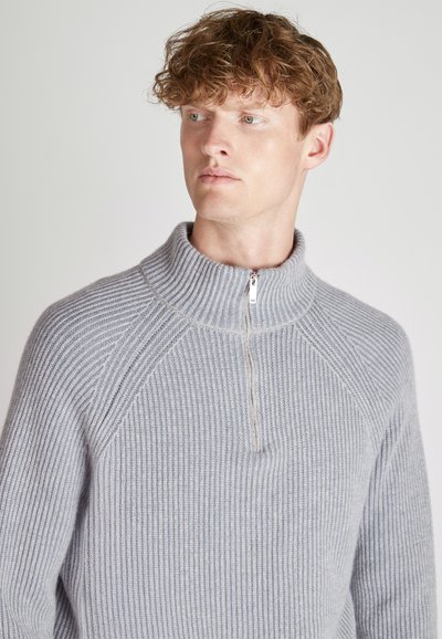 Hellgrauer Zip-Hals-Pullover mit gerippter Textur, hoher Kragen und Raglanärmeln, aus weichem Material hergestellt.