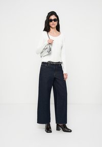 Λευκό ριγωτό μακρυμάνικο τοπ, ψηλόμεσο σκούρο μπλε τζιν με φαρδιά μπατζάκια, ασημένια ζώνη με τρουκς, διάφανη τσάντα και μαύρες γυαλιστερές γόβες.