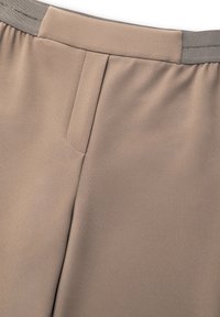 Beżowe spodnie o gładkiej fakturze, z płaskim przodem i elastycznym pasem w kontrastowym szarym kolorze.