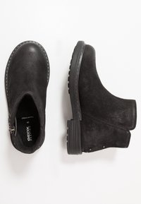 Svarta mockastövlar med rund tå, sidodragkedja och texturerad gummisula. Har sömnadsdetaljer och en minimalistisk design.