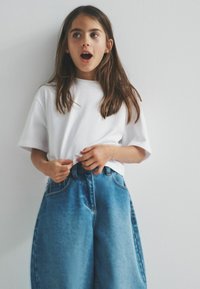 Weißes Baumwoll-T-Shirt mit kurzen Ärmeln, kombiniert mit hochgeschnittenen, locker sitzenden Jeans aus Denim in einer hellblauen Waschung und sichtbaren Stichdetails.
