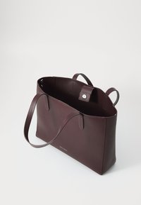 Sac fourre-tout en cuir bordeaux avec un extérieur texturé, deux poignées robustes et une fermeture à pression. Son design ouvert met en valeur un espace intérieur spacieux.