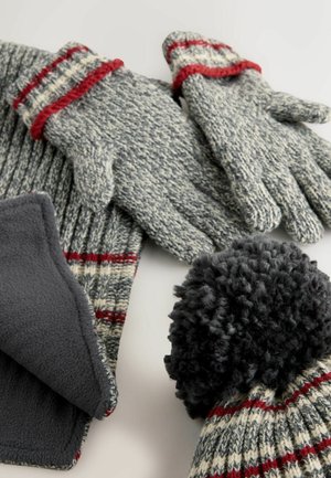 Adīti pelēki cimdi, šalle un cepure ar sarkanām svītrām; cepurei ir melns pom-poms. Mīksta tekstūra, kontrastējoši materiāli un krāsas.