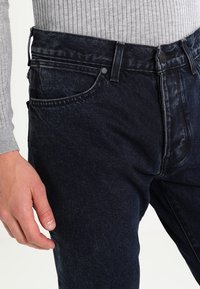 Mörkblå denimjeans med slim fit, med framfickor, knappstängning och subtilt blekt mönster på tyget.