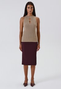 Beige ribbeltop zonder mouwen met keyhole uitsnijding, in combinatie met een aansluitende bordeauxrode rok tot de knie, gedragen met puntige bordeauxrode hakken.