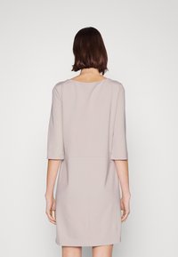 Beige klänning med avslappnad passform, rund halsringning och trekvartslånga ärmar. Slät textur utan synliga mönster eller detaljer.