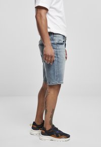Lyseblå denim shorts med lige pasform, frayed kant og fem-lomme design. Bæres med sorte og brune træningssko.