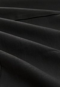 Černá látka s hladkou, matnou texturou, zobrazující záhyby a linie, která prezentuje elegantní, jednotný vzhled bez vzorů nebo akcentů.