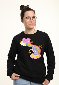 Sudadera negra con un gráfico multicolor de dos osos de dibujos animados en nubes, con un arcoíris y estrellas amarillas en el diseño.