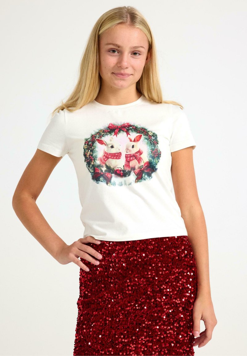 Hvid t-shirt med kortærmer, der har et festligt kaninmotiv omgivet af en grøn krans. Båret med en skinnende rød pailletnederdel.