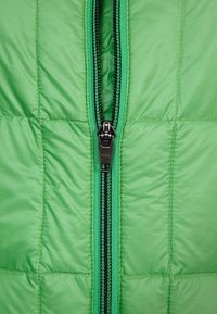 Zelená prošívaná bunda s celým černým zipem se zelenými detaily, která předvádí hladkou texturu a jednotný vzor na celé látce.