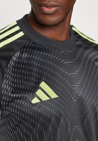 T-shirt de sport noir avec un design texturé, présentant des rayures vert jaune vif sur les épaules et un logo Adidas brodé.